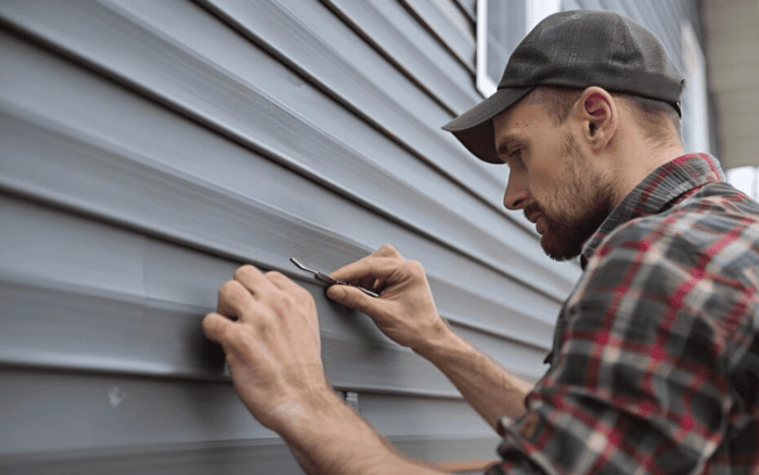 A man repairing house siding, demonstrating home maintenance skills.